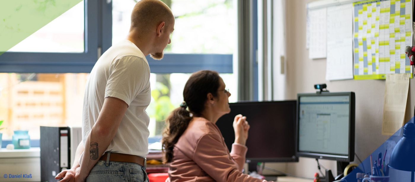 Das Bild zeigt einen Freiwilligen mit einer Lehrerin beim Planen am Computer.
